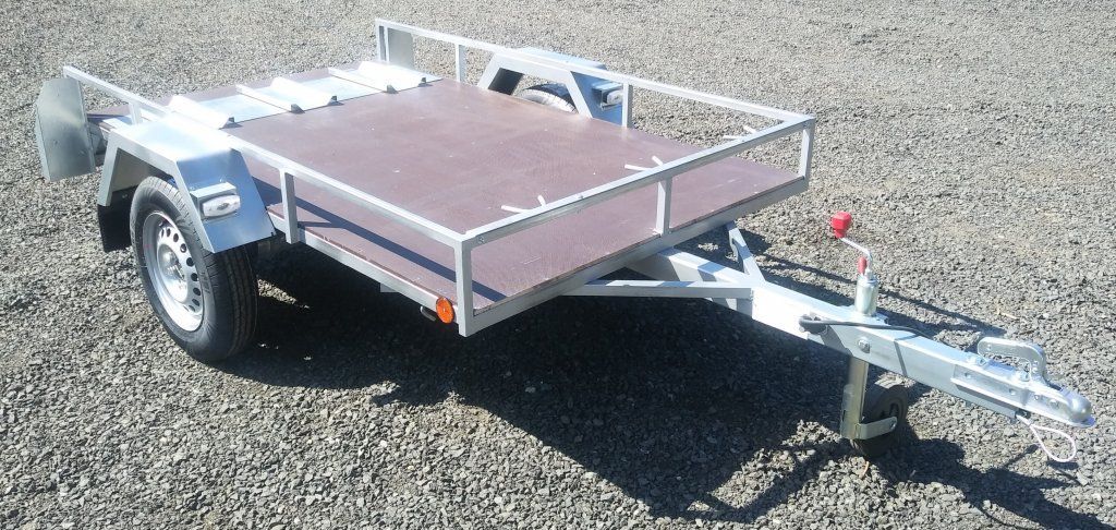 Un pequeño remolque con plataforma de madera está estacionado sobre grava.