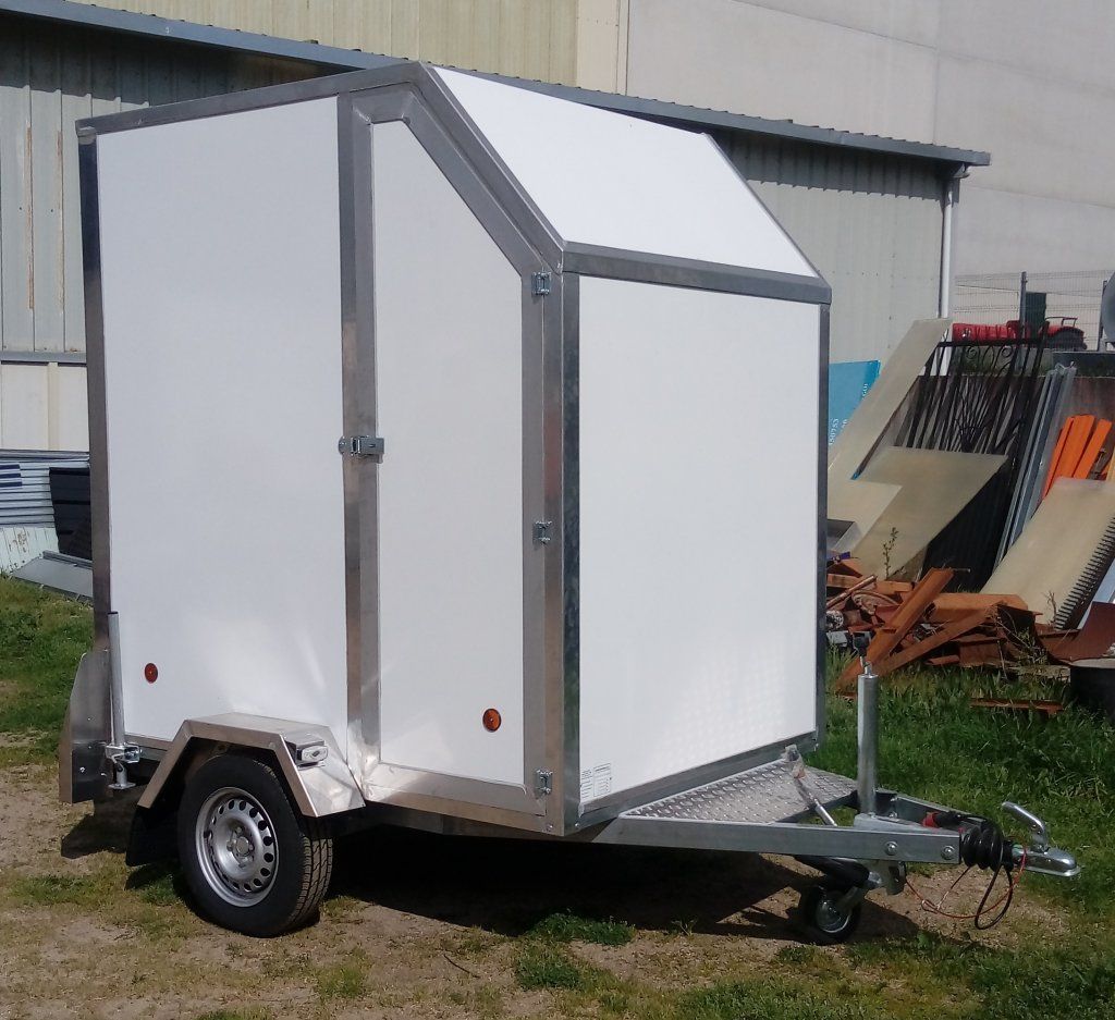 Un remolque blanco está estacionado en el césped frente a un edificio.
