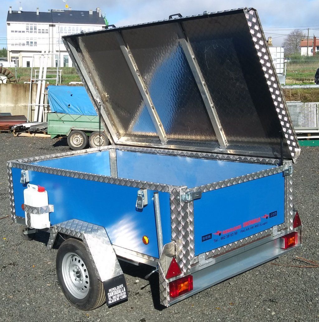 Un remolque azul con la tapa abierta está estacionado en un lote de grava.