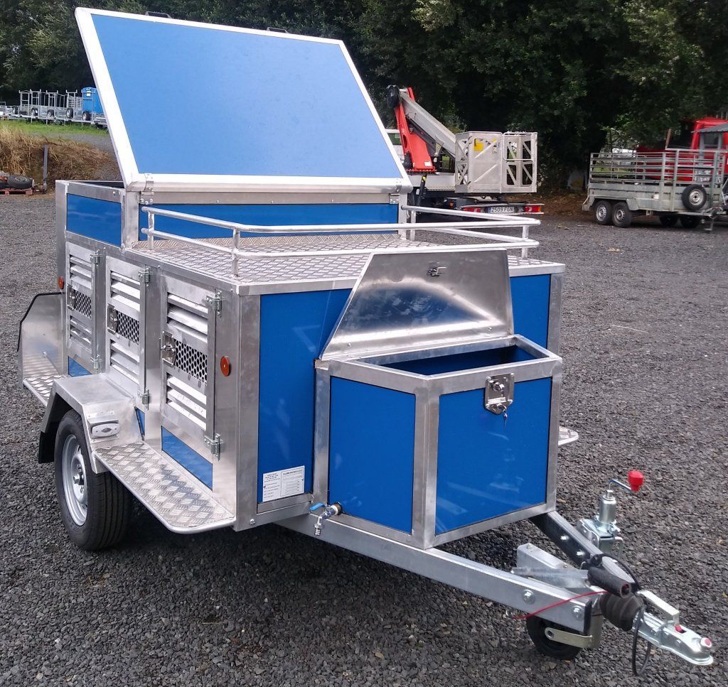 Un remolque azul y plateado está estacionado en un lote de grava.