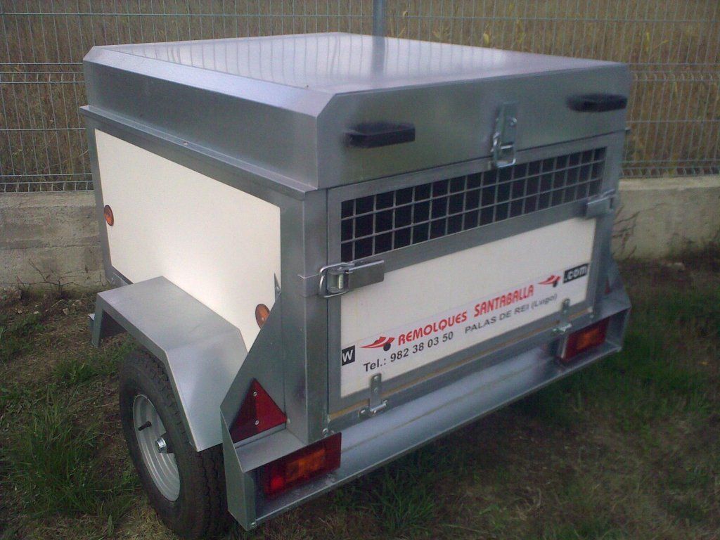 Un remolque con una jaula en la parte trasera está estacionado en el césped.