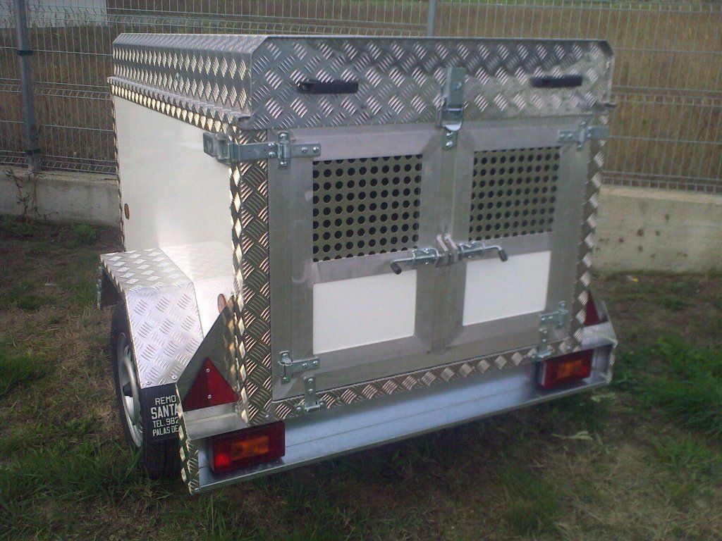 Un remolque con una jaula en la parte trasera está estacionado en el césped.