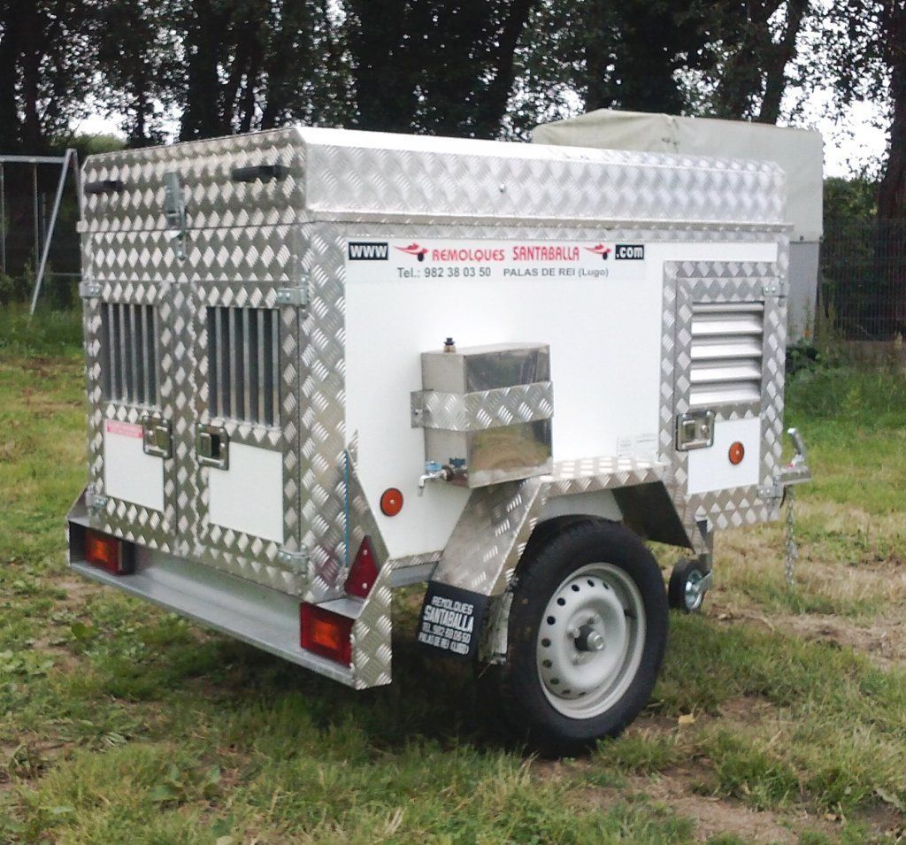 Un remolque blanco con una jaula de acero inoxidable en la parte superior está estacionado en el césped.