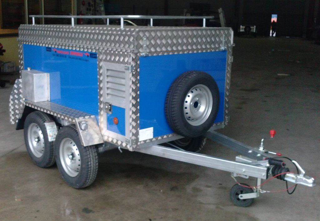 Un remolque azul y plateado con una llanta de repuesto en la parte trasera.