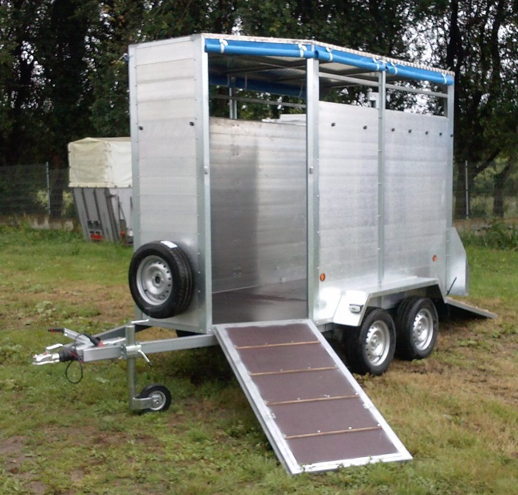 Un remolque plateado con una rampa en el lateral está estacionado en un campo de hierba.