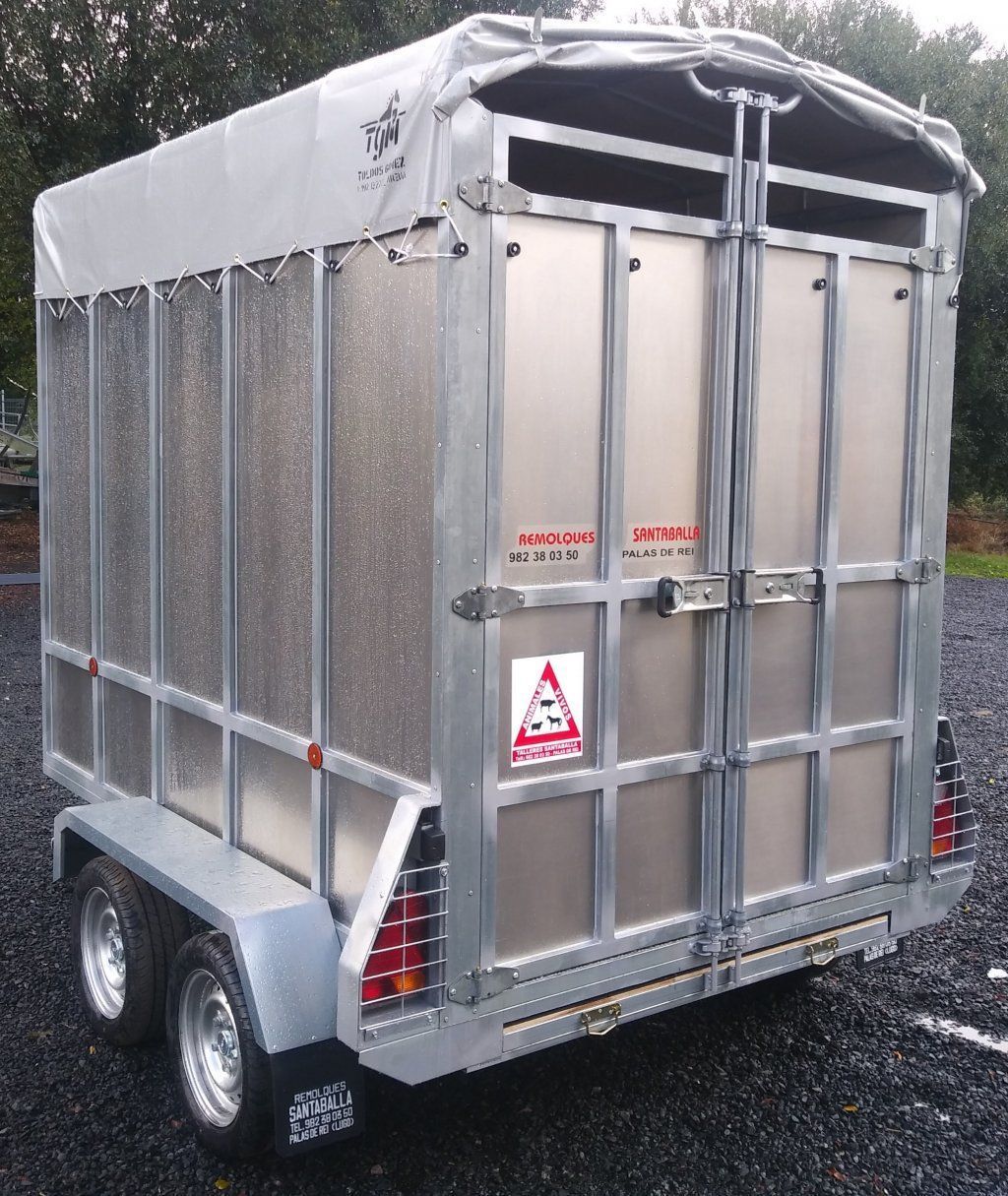 Un remolque plateado con una lona blanca encima está estacionado en un lote de grava.