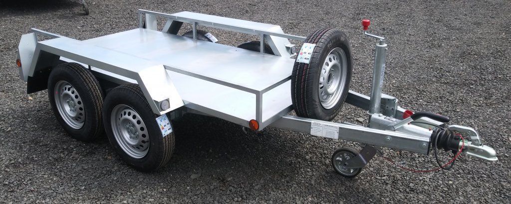 Un pequeño remolque con dos ruedas está estacionado sobre grava.