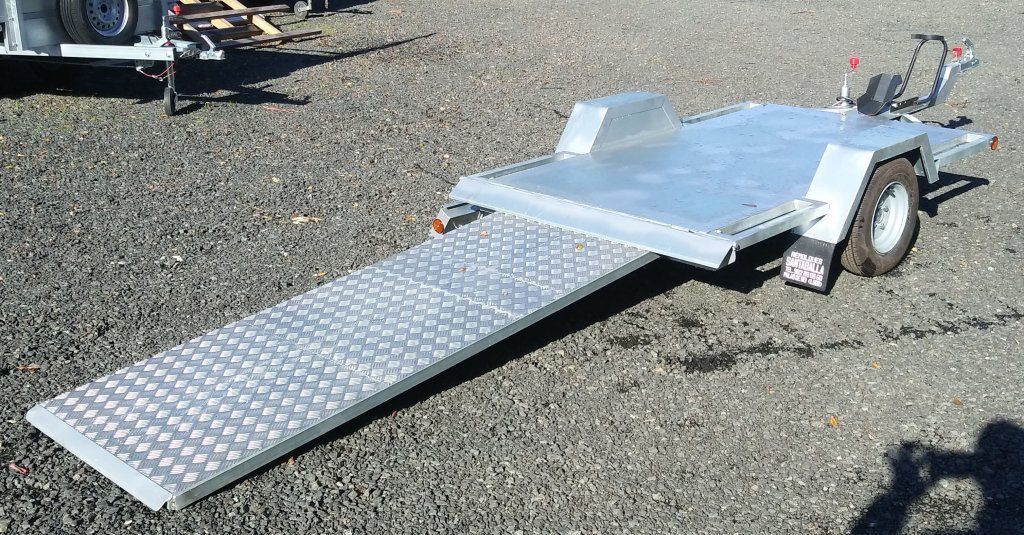 Un remolque con una rampa acoplada está estacionado sobre grava.