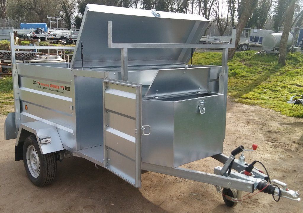 Un remolque de metal con una caja en la parte trasera está estacionado en un camino de tierra.