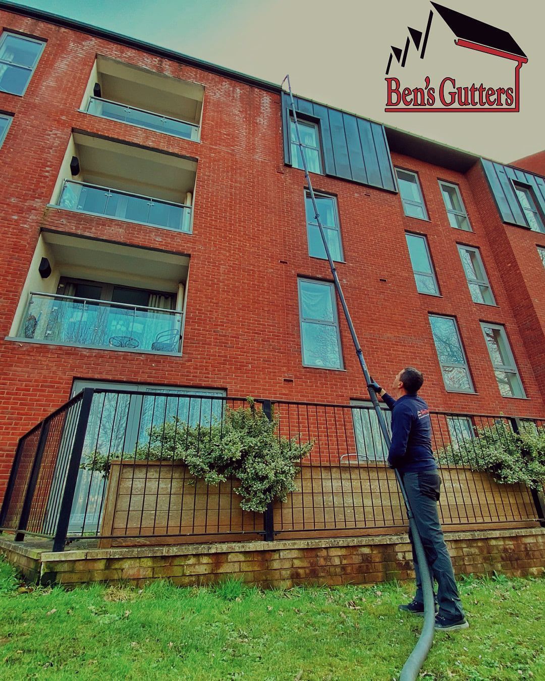 Person stands on a grassy lawn beside a red brick building with balconies and a sign reading “Ben’s Guest.”