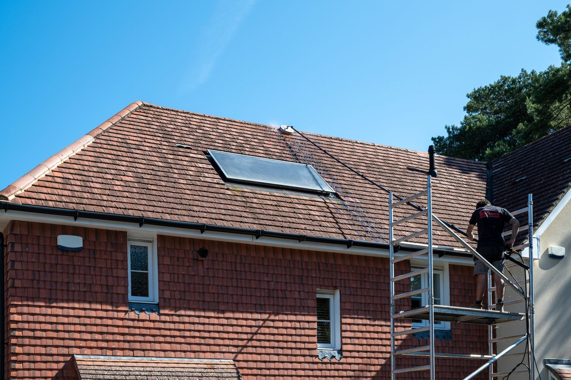 Red tiled roof with skylight on a brick house, with scaffolding on the right.