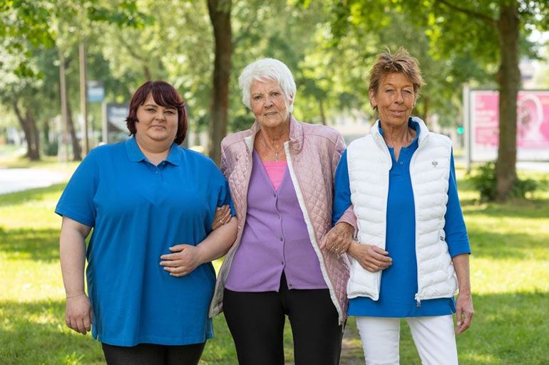 Eine Krankenschwester gibt einer älteren Frau im Rollstuhl einen Apfel.