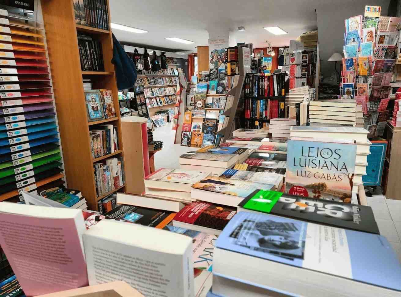 Pasillo de librería con pilas de libros y revistas, incluyendo un expositor de “Letos Lituania” en primer plano.