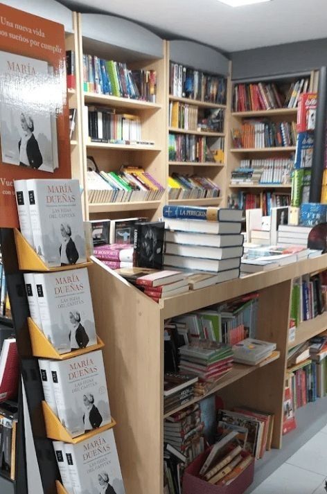 Mostrador de una pequeña librería con libros apilados y estanterías llenas de libros coloridos al fondo.