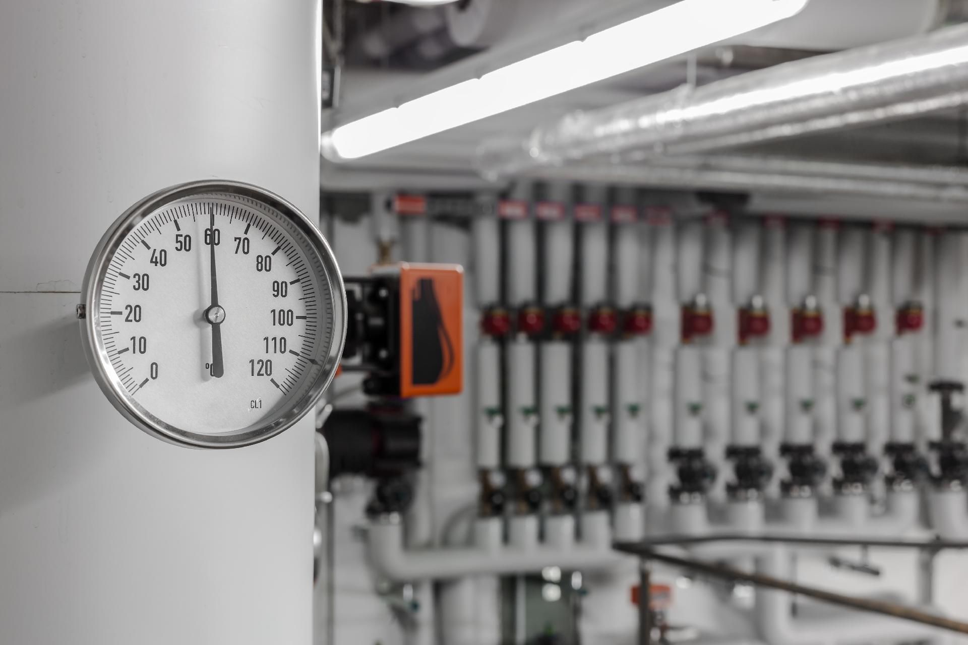 Manometer an einer Rohrleitung in einer Industrieanlage mit Ventilen und Maschinen im Hintergrund