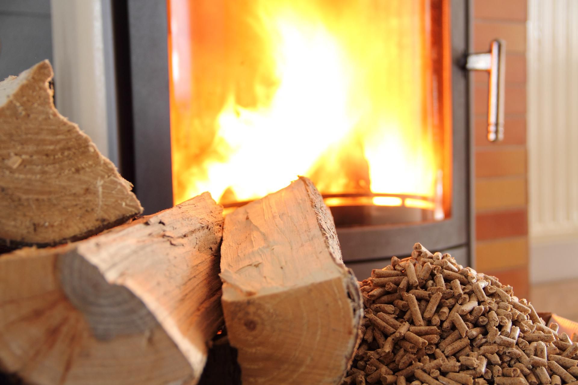 Holzscheite und Holzpellets brennen in einem Kamin mit hellorangefarbenen Flammen.
