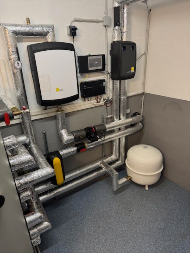 Hauswirtschaftsraum mit Warmwasserbereiter, Schwarz-Weiß-Tank und Rohren in einem schmalen Abstellraum