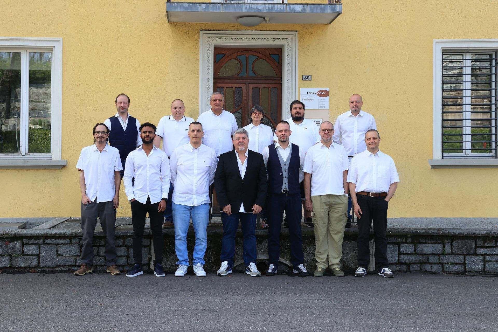 Un gruppo di uomini posa per una foto davanti a un edificio giallo.