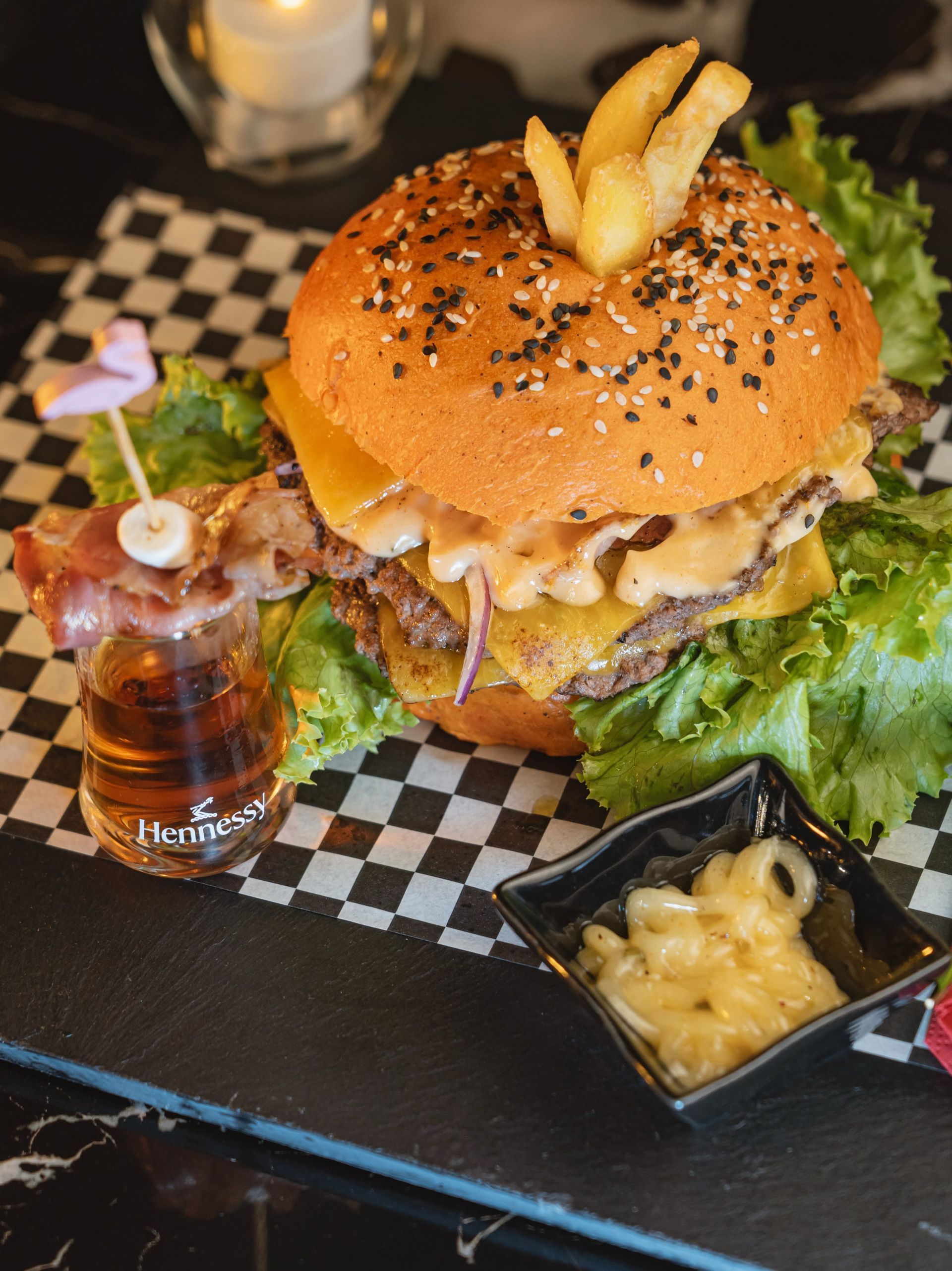 Burger servi sur un plateau à carreaux avec frites, laitue, boisson et une sauce au fromage fondu en accompagnement.