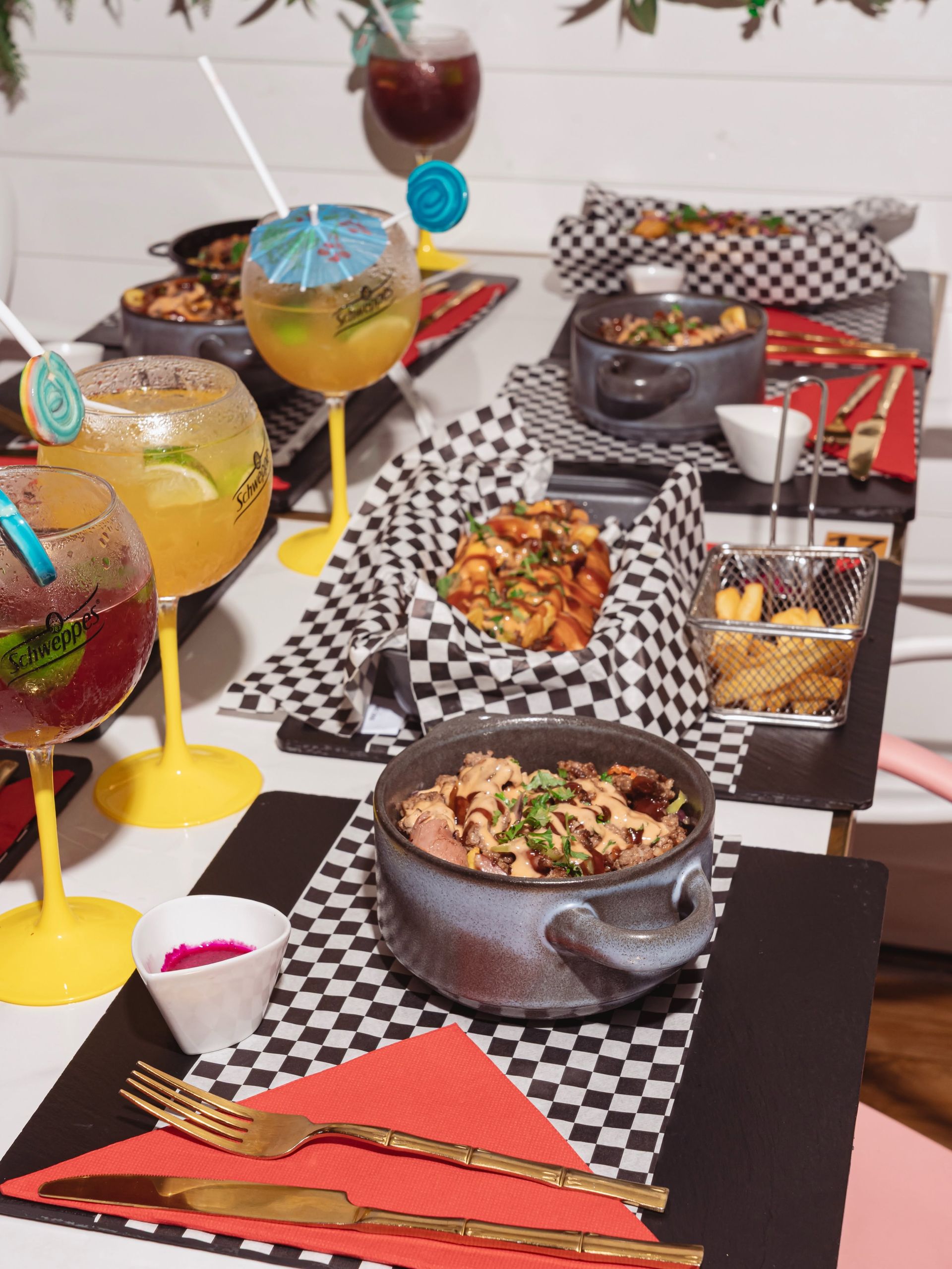 Élégante présentation de cocktails colorés et de petits amuse-bouche sur des chemins de table à carreaux noirs et blancs.