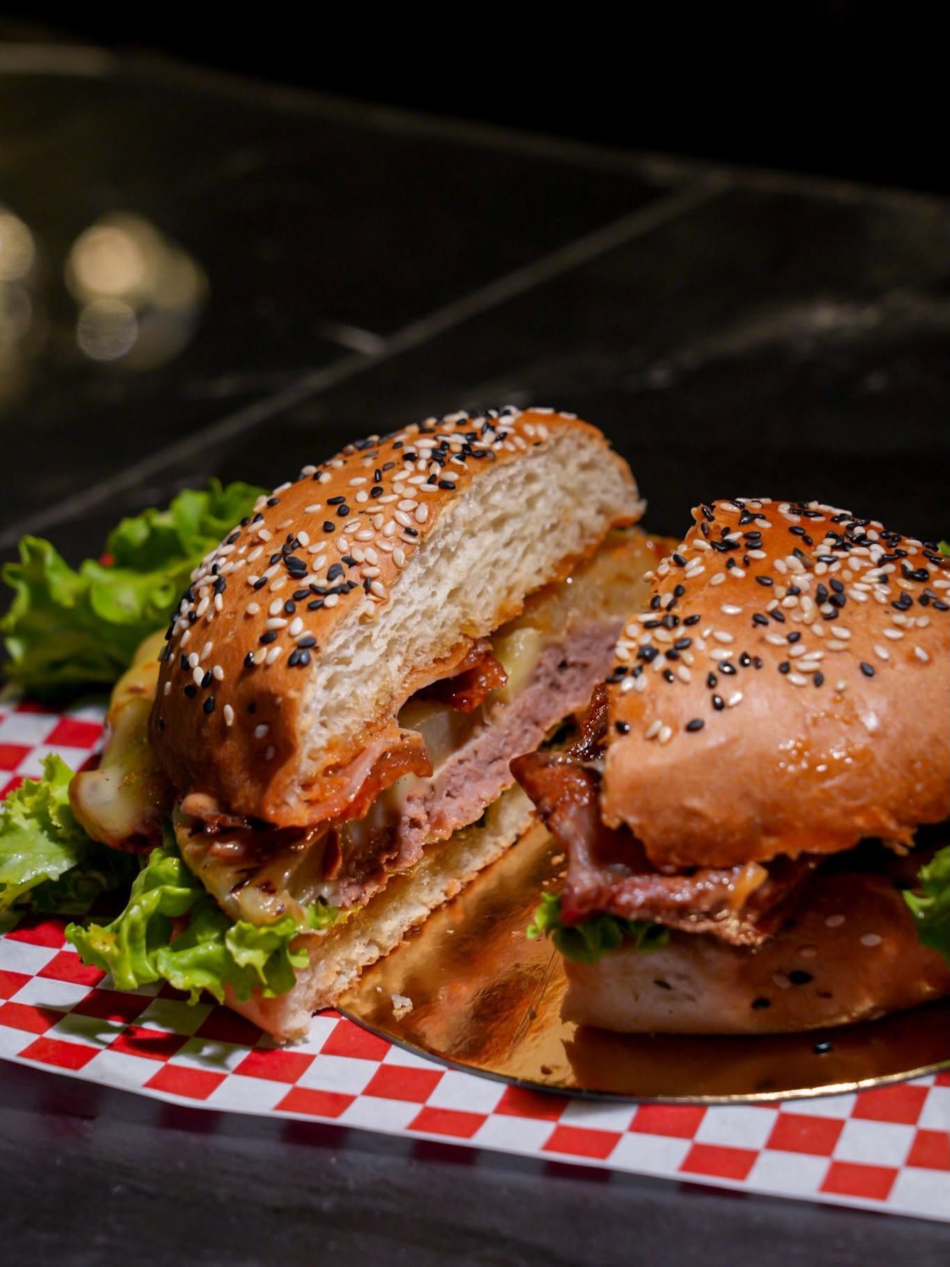 Sandwich hamburger avec pain au sésame sur un plateau recouvert de papier à carreaux, avec laitue et bacon visibles
