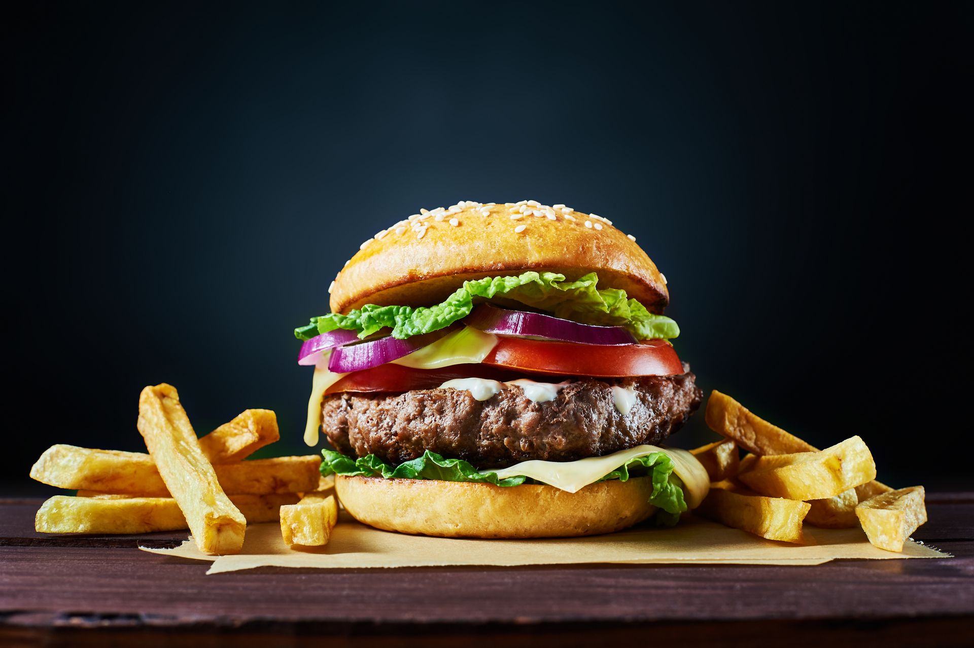 Hamburger juteux avec laitue, tomate, oignon et frites sur fond sombre.