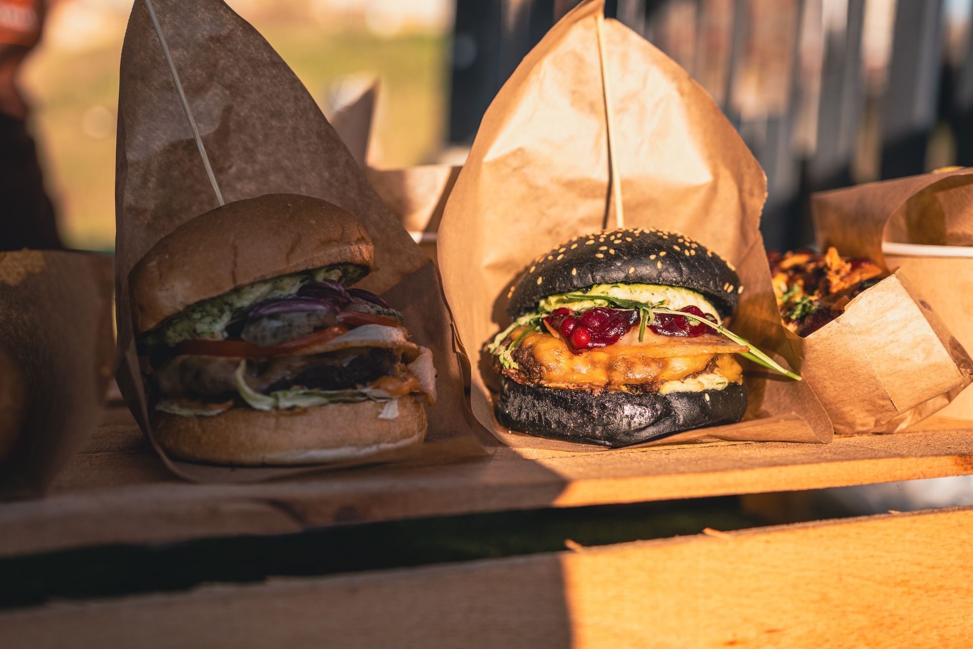 Deux hamburgers gastronomiques dans des sacs en papier brun sur une table en bois, éclairée par la douce lumière du soleil.