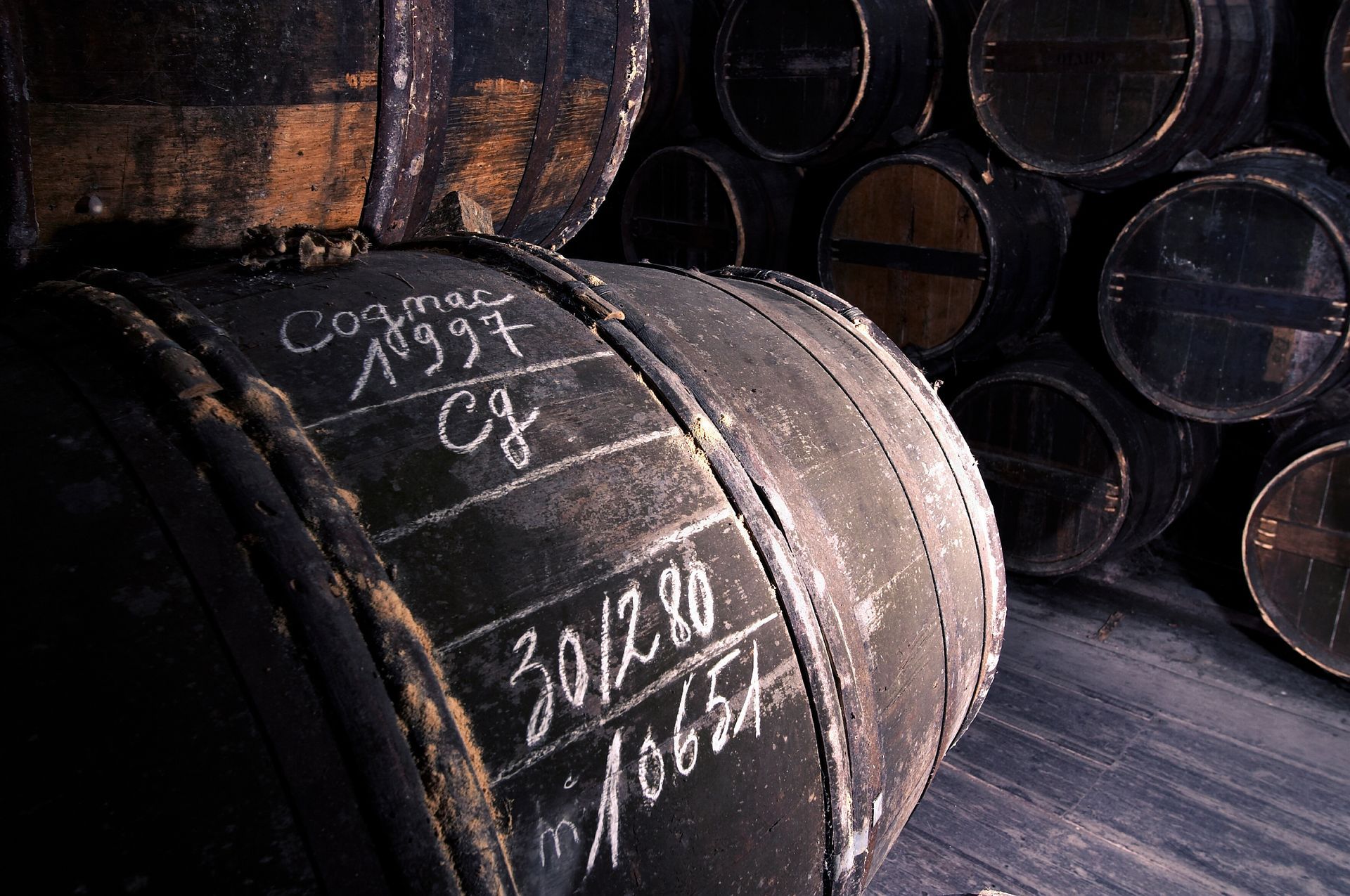 Des tonneaux en bois empilés dans une cave sombre, l'un d'eux marqué à la craie de dates et de notes.