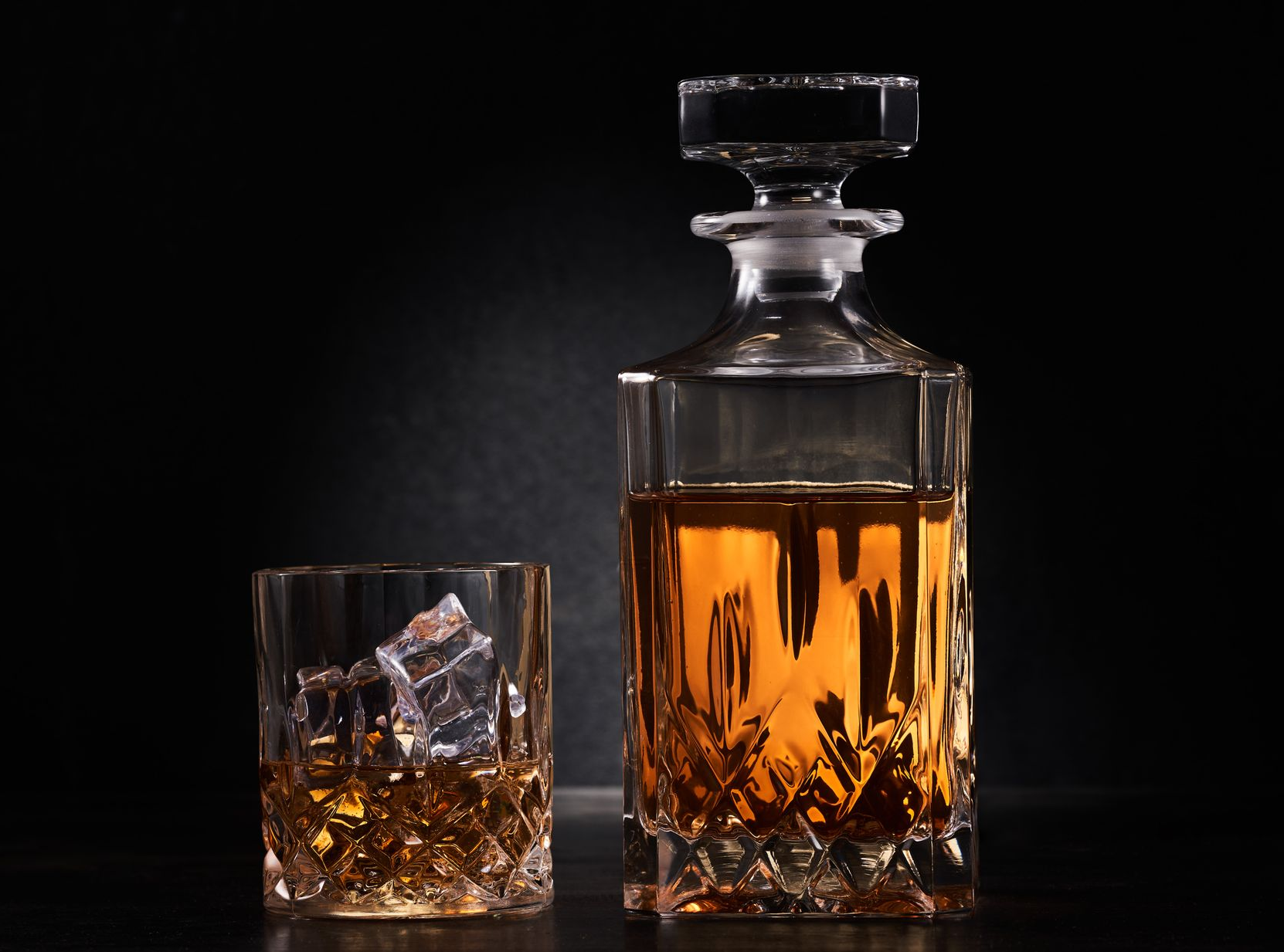 Carafe à whisky et verre à whisky avec des glaçons sur fond sombre.