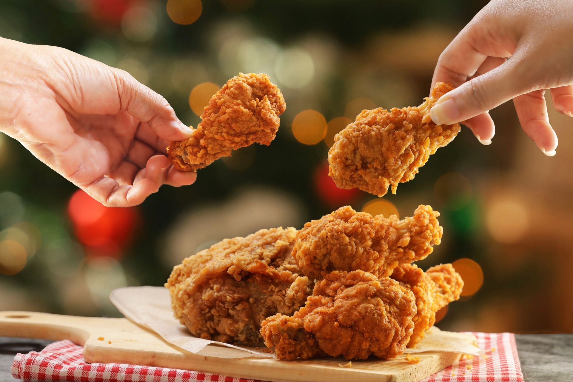 Des mains se tendent vers des morceaux de poulet frit croustillants sur une assiette à une table de fête.