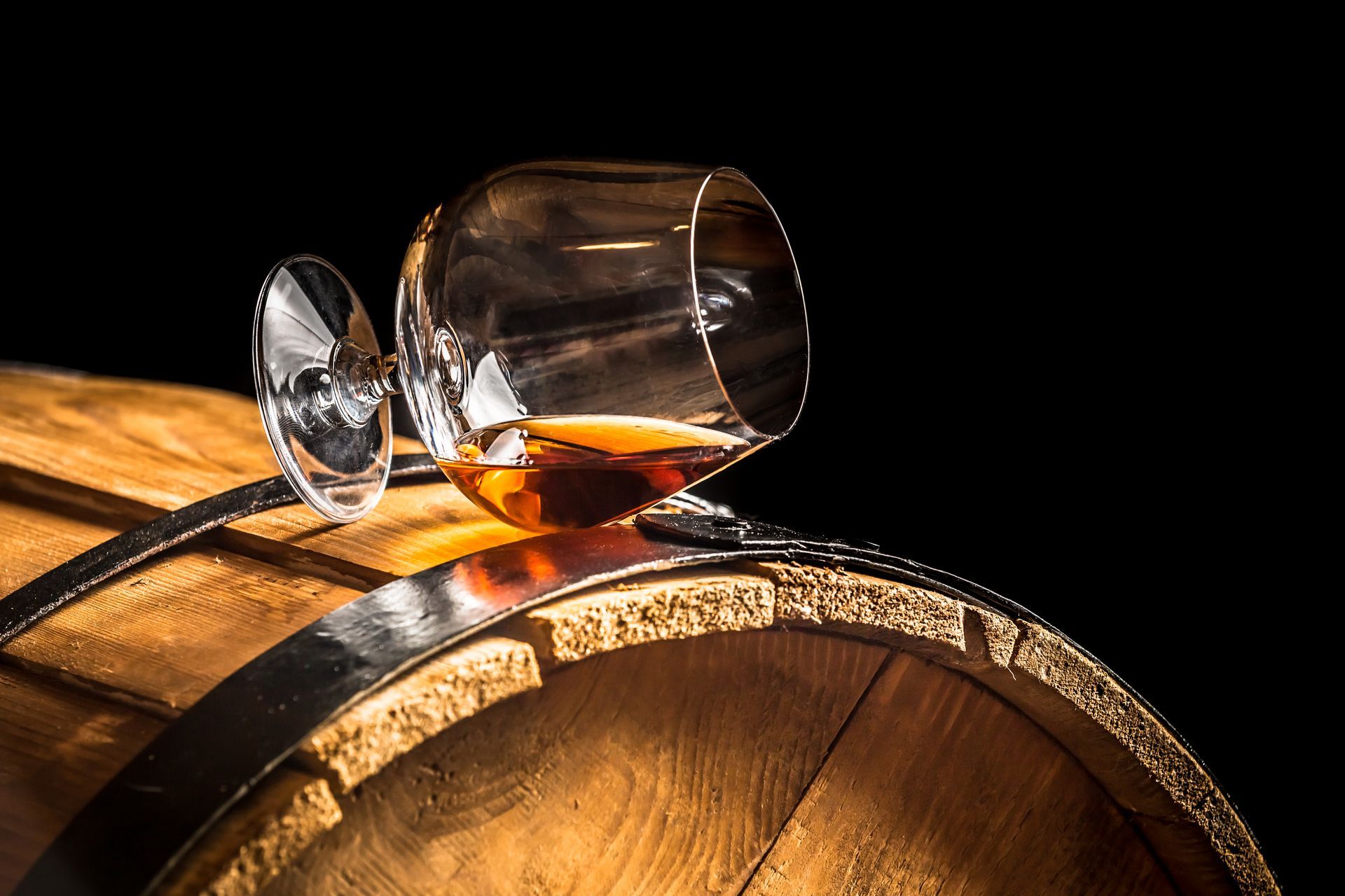 Une liqueur ambrée renversée sur un tonneau en bois, avec un verre renversé dessus.