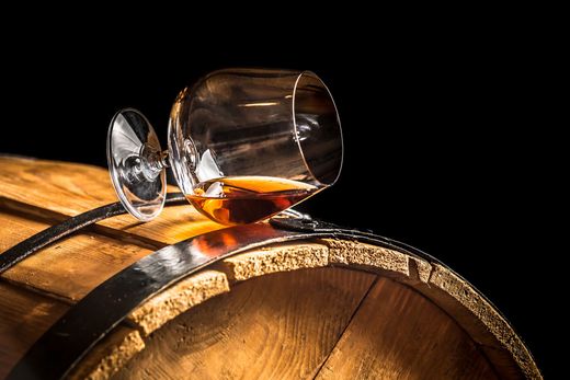 Une liqueur ambrée renversée sur un tonneau en bois, avec un verre renversé dessus.