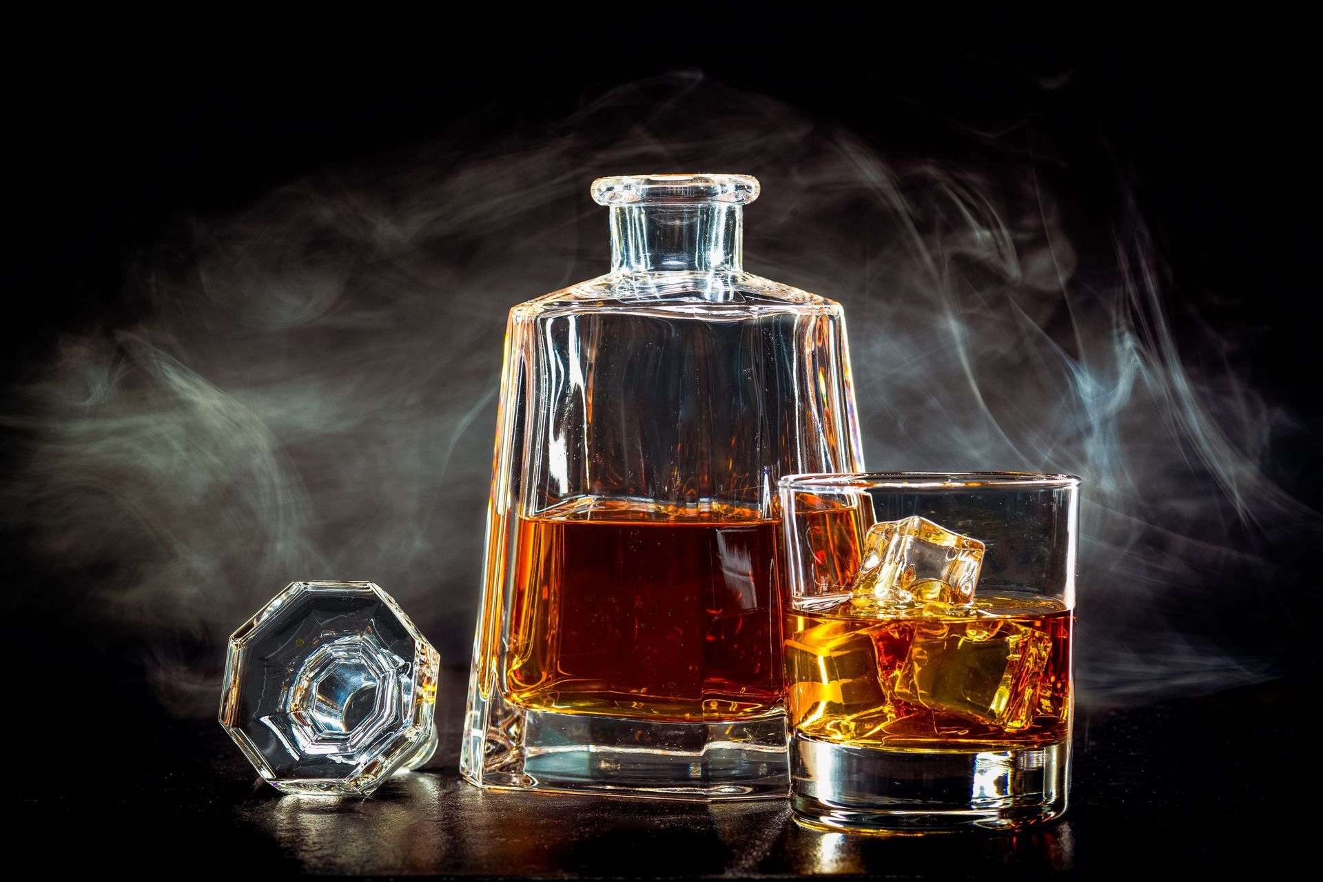 Carafe à whisky et verre contenant une liqueur ambrée sur un fond sombre et fumé.