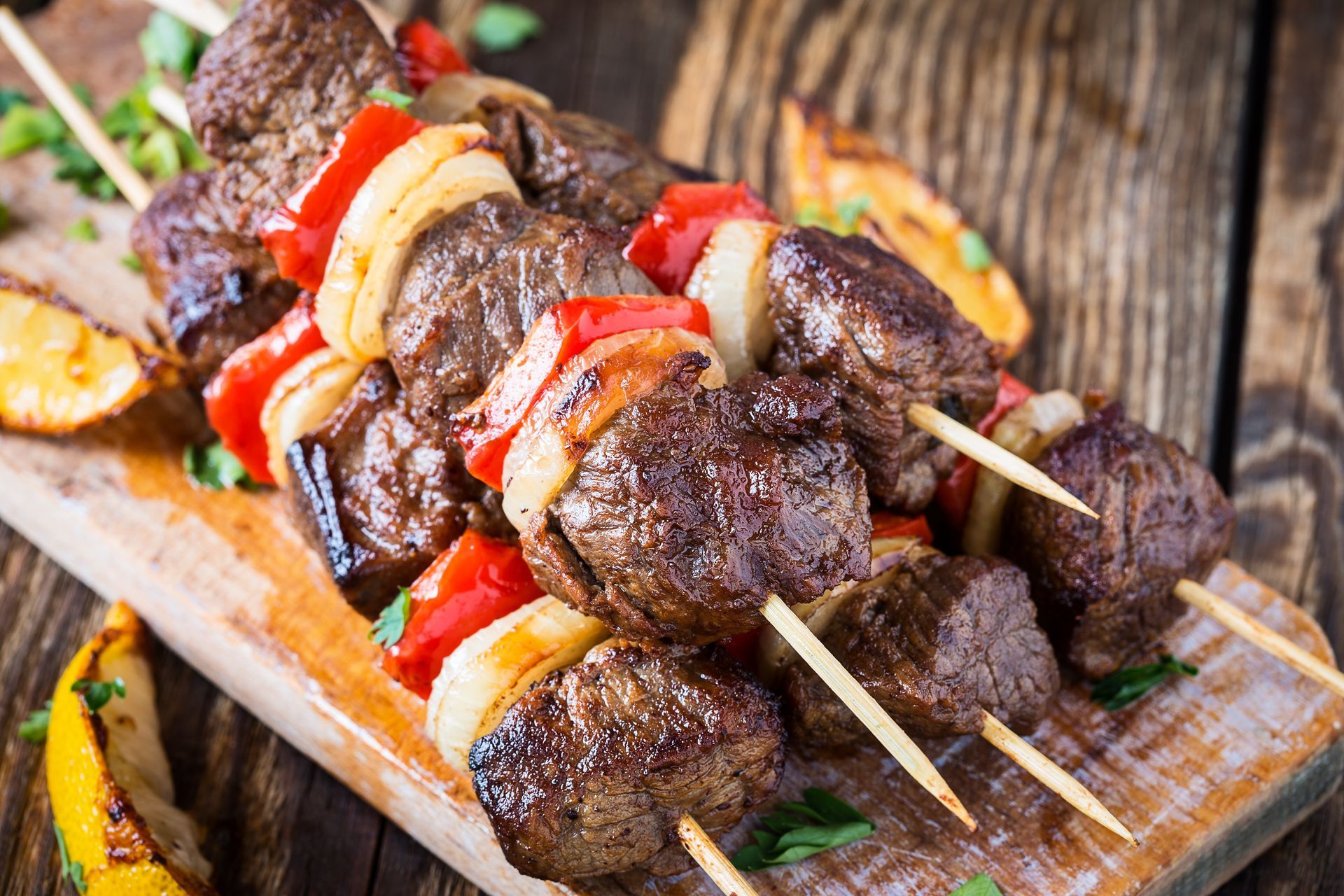 Brochettes de bœuf grillées aux poivrons rouges et jaunes sur une planche en bois.
