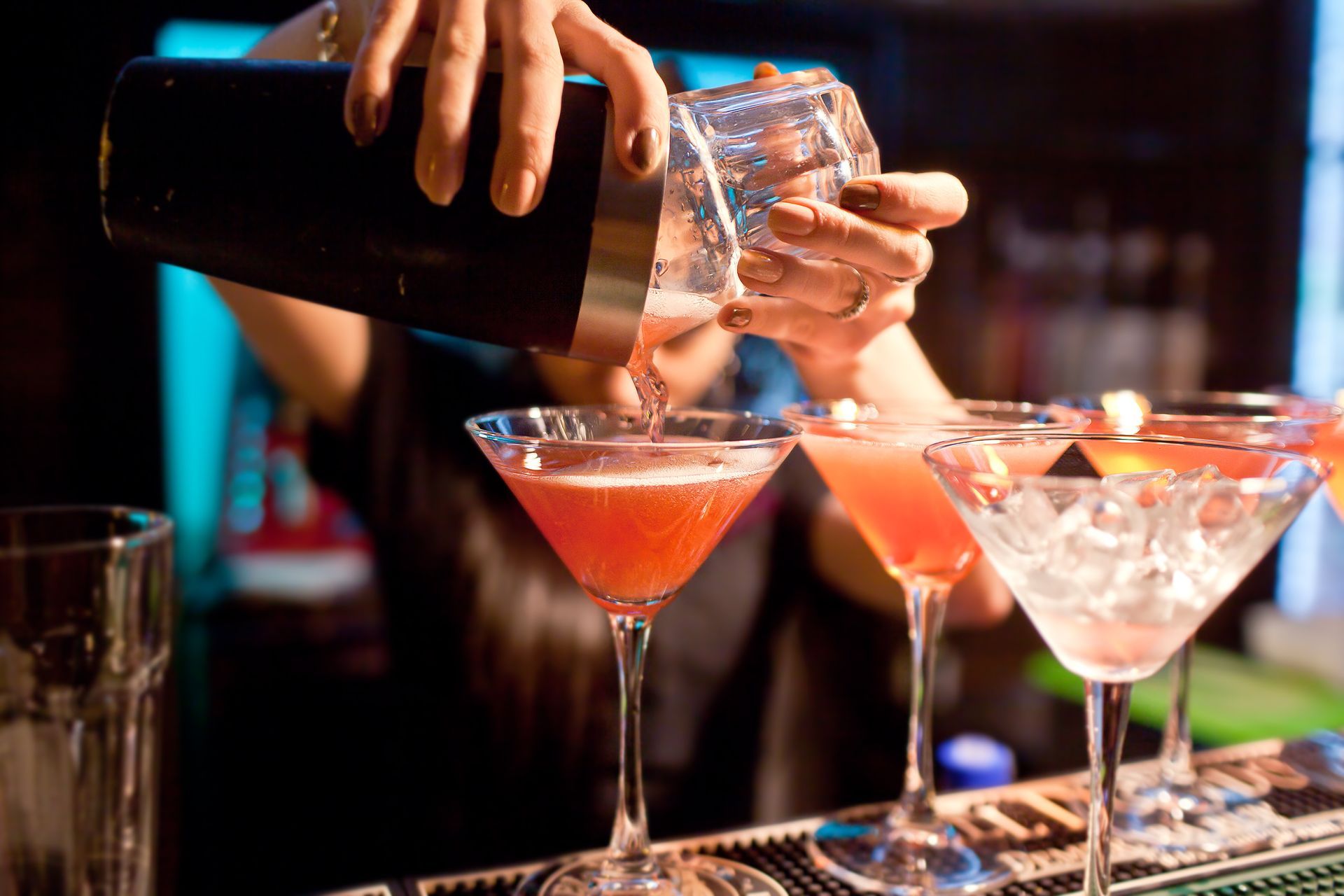 Un barman verse un cocktail d'un shaker dans des verres à martini dans un bar.