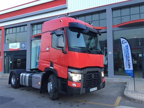 Un camión semirremolque rojo está estacionado frente a un edificio.