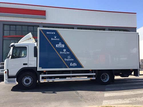 Un camión blanco con una franja azul en el costado está estacionado frente a un edificio.