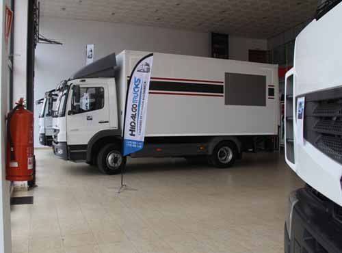 Un camión blanco está estacionado en una sala de exposición al lado de un extintor de incendios.