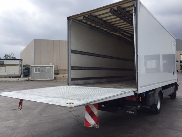 Una camioneta blanca con la puerta trasera abierta está estacionada en un estacionamiento.