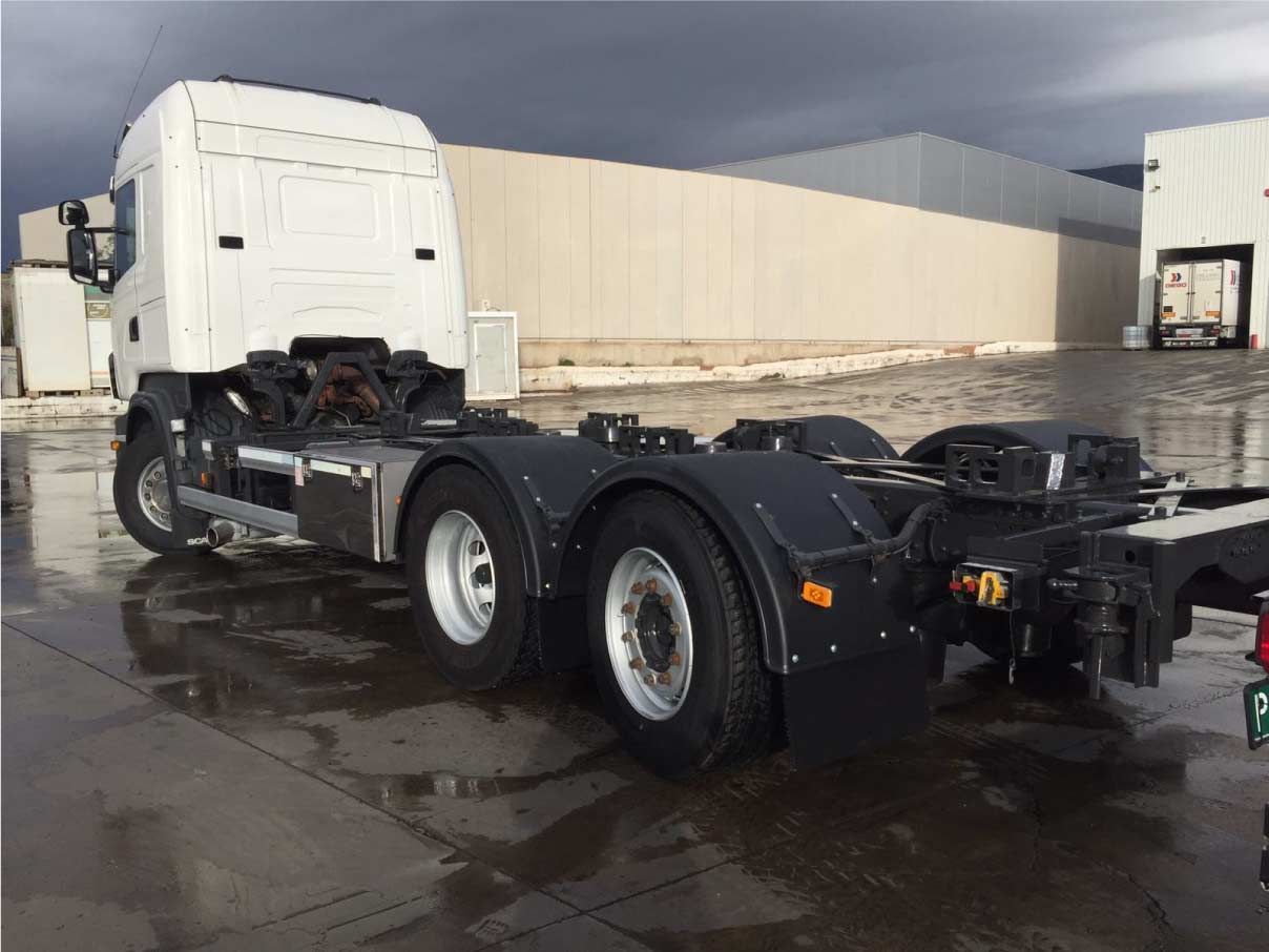 Un camión semirremolque blanco está estacionado en un estacionamiento frente a un edificio.