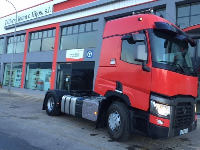 Un camión semirremolque rojo está estacionado frente a un edificio.