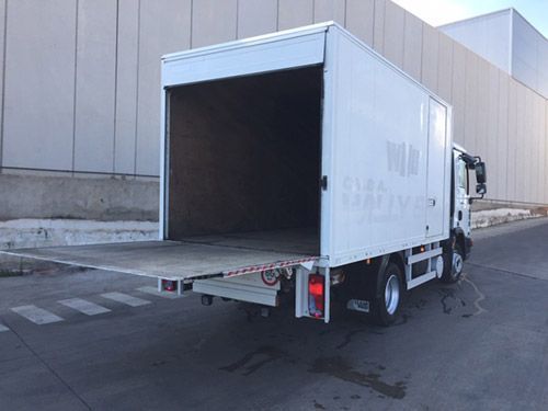 Un camión blanco con la puerta trasera abierta está estacionado frente a un edificio.