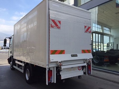 Un camión blanco con un elevador en la parte trasera está estacionado frente a un edificio.
