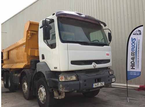 Un camión de volteo está estacionado frente a un edificio al lado de una bandera.