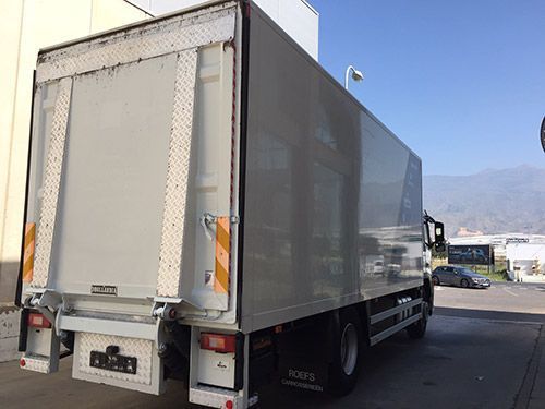 Un camión blanco con un elevador en la parte trasera está estacionado en un estacionamiento.