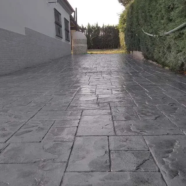 Un camino de ladrillo que conduce a una casa con un seto al fondo.