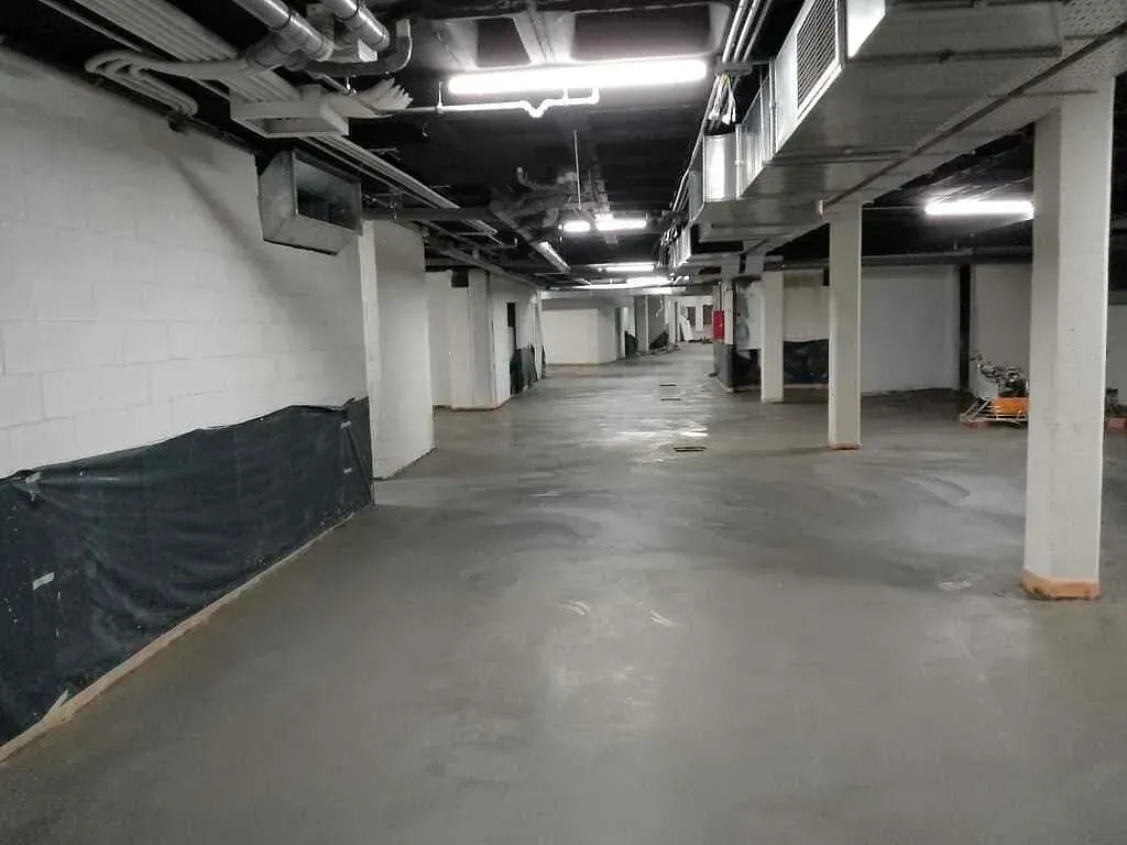 Un estacionamiento subterráneo vacío con pisos de concreto y paredes blancas.