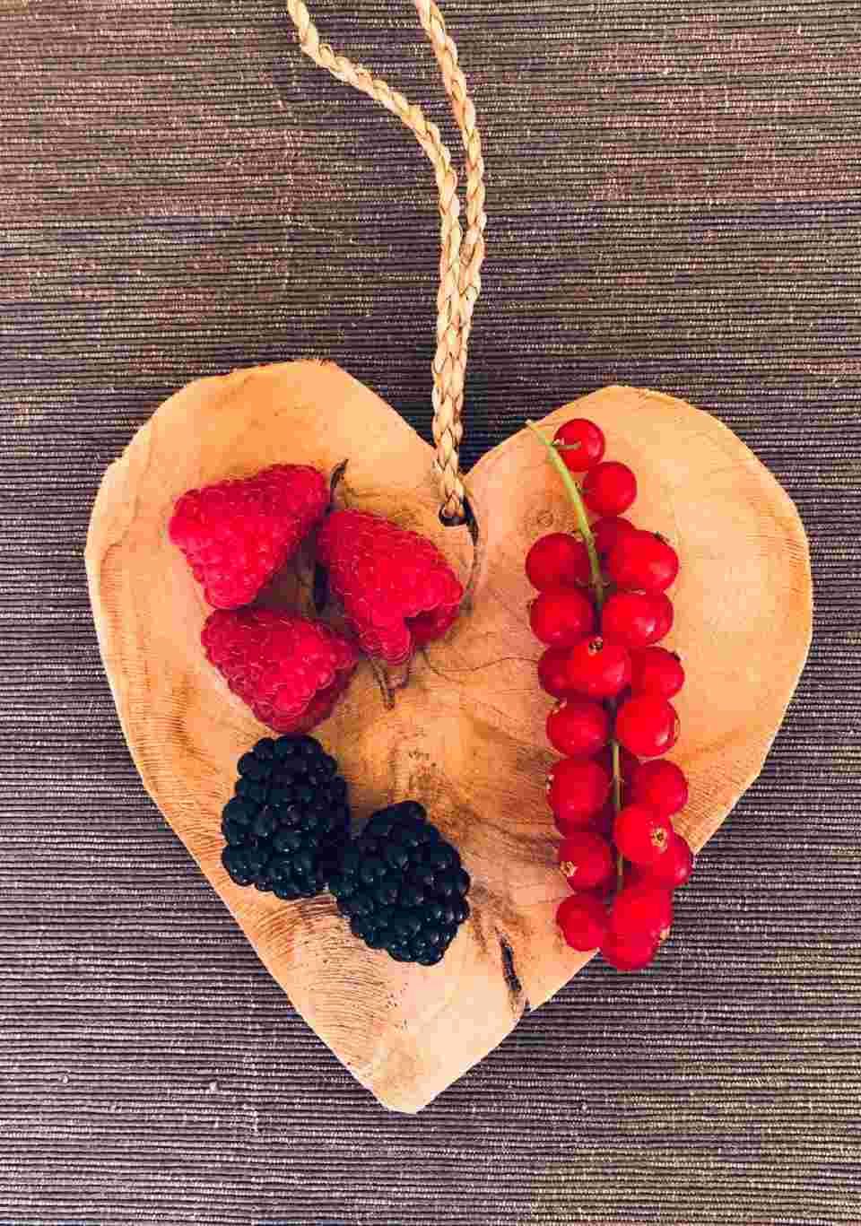 Herz aus Holz mit frischen Himbeeren, Brombeeren und roten Johannisbeeren