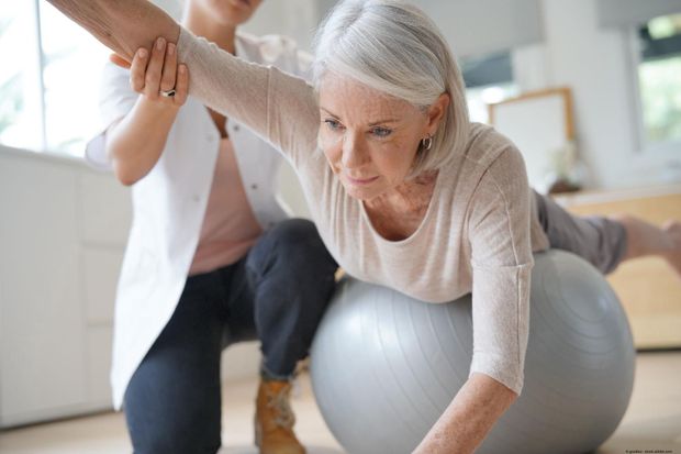 Seniorin bei Krankengymnastik auf Gymnastikball mit Physiotherapeutin