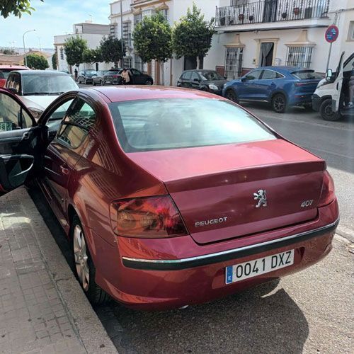 Un Peugeot 407 rojo está estacionado en una calle frente a unos edificios. La puerta del conductor está abierta.